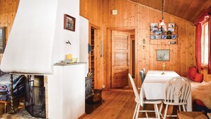 Un intérieur de chalet chaleureux avec une cheminée, des murs en bois, un coin repas avec une table et des chaises, et une étagère ornée d’objets décoratifs.