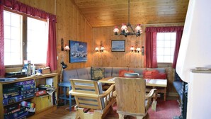 L’intérieur chaleureux d’un chalet avec des murs en bois, un canapé, une table à manger et une bibliothèque remplie de jeux de société.