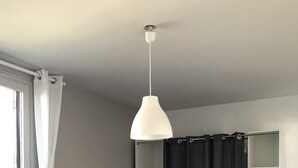 A room with a bed, a chair, a wardrobe, a hanging light fixture, and a window with curtains. - Beautiful apartment in the center of Anglet, 10 minutes from the beach (anglet)