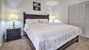 A neatly made bed with a white duvet, two bedside tables with lamps, a dark wooden headboard, a wall-mounted picture, and a large closet with louvered doors. - Maryland Vacation Home Near US Capital! (Riverdale Park)