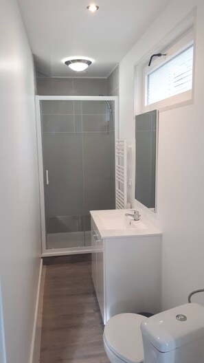 A narrow bathroom with a shower, toilet, and sink.
