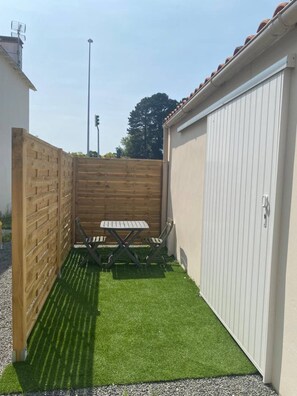 A small outdoor patio with a table and chairs, surrounded by a wooden fence and a white garage door.
