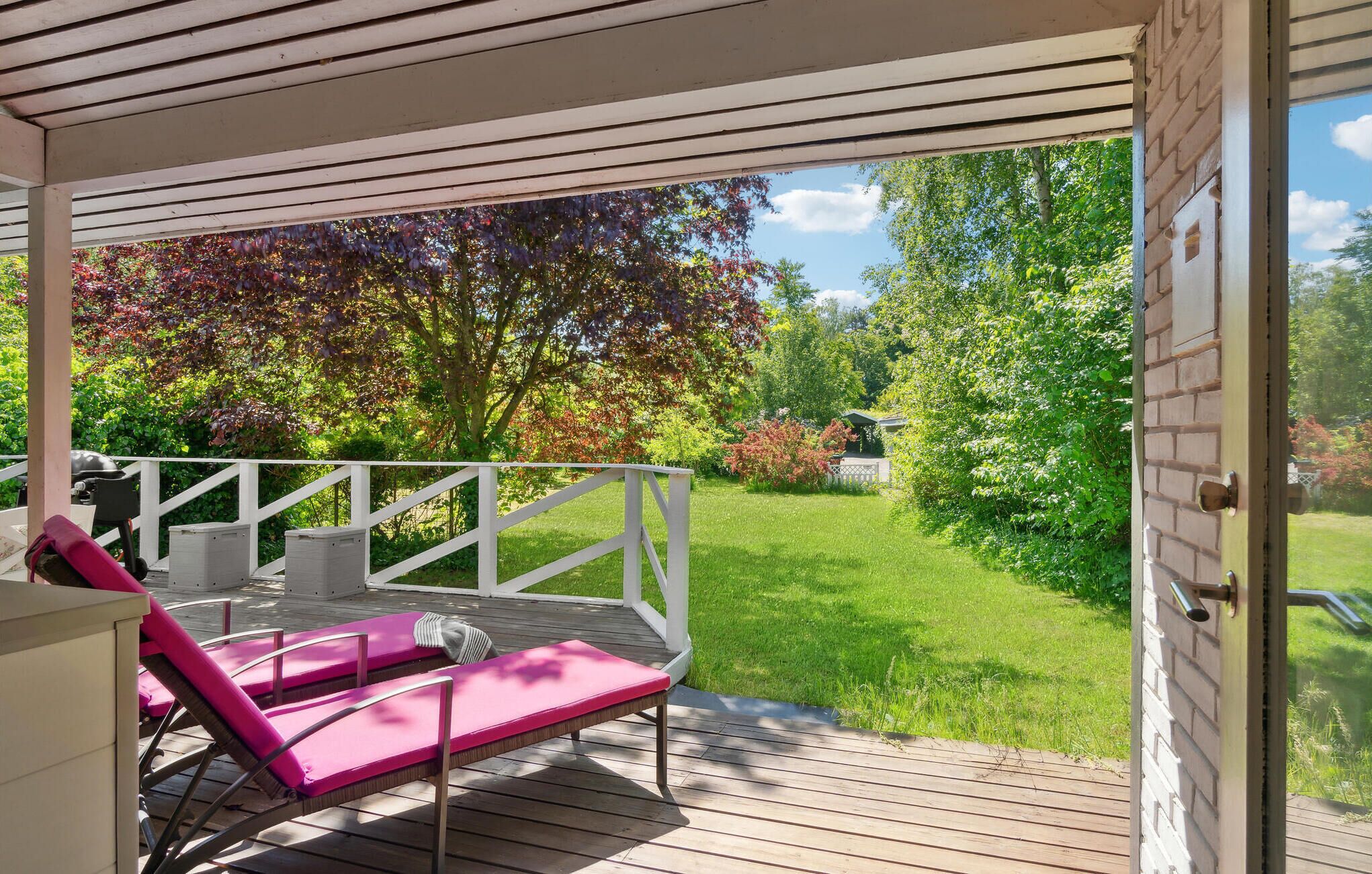 A covered outdoor area with a wooden deck, a white railing, and two pink lounge chairs.