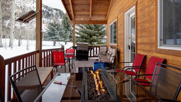 A wooden cabin with a covered porch, outdoor seating, a fire pit, and a view of snow-covered trees and mountains. - Where Greater Yellowstone adventures begin. (Star Valley Ranch)