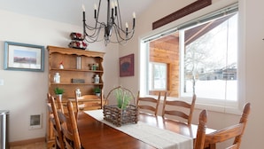 A wooden dining table with chairs, a chandelier, and a window with a view of a snowy landscape. - Where Greater Yellowstone adventures begin. (Star Valley Ranch)