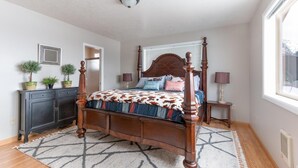 A four-poster bed with a patterned bedspread, a dark wooden dresser with potted plants, and a window with blinds. - Where Greater Yellowstone adventures begin. (Star Valley Ranch)