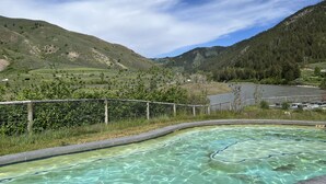 A swimming pool with clear water, surrounded by a wire fence, set against a backdrop of green hills and a mountain. - Where Greater Yellowstone adventures begin. (Star Valley Ranch)