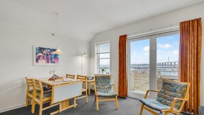 A room with a dining table, chairs, a painting, and a large window with curtains. - Stunning apartment in Rudkøbing (Rudkøbing)