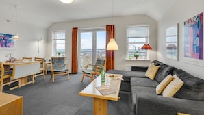 A modern living room with a grey sofa, wooden coffee table, and a dining area with a table and chairs. Large windows offer views of the sea and a bridge. - Stunning apartment in Rudkøbing (Rudkøbing)