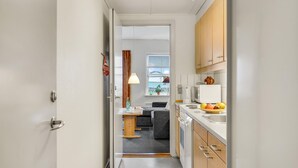 A narrow hallway leading to a compact kitchen with a dining area, a window with a view, and a small seating area. - Stunning apartment in Rudkøbing (Rudkøbing)