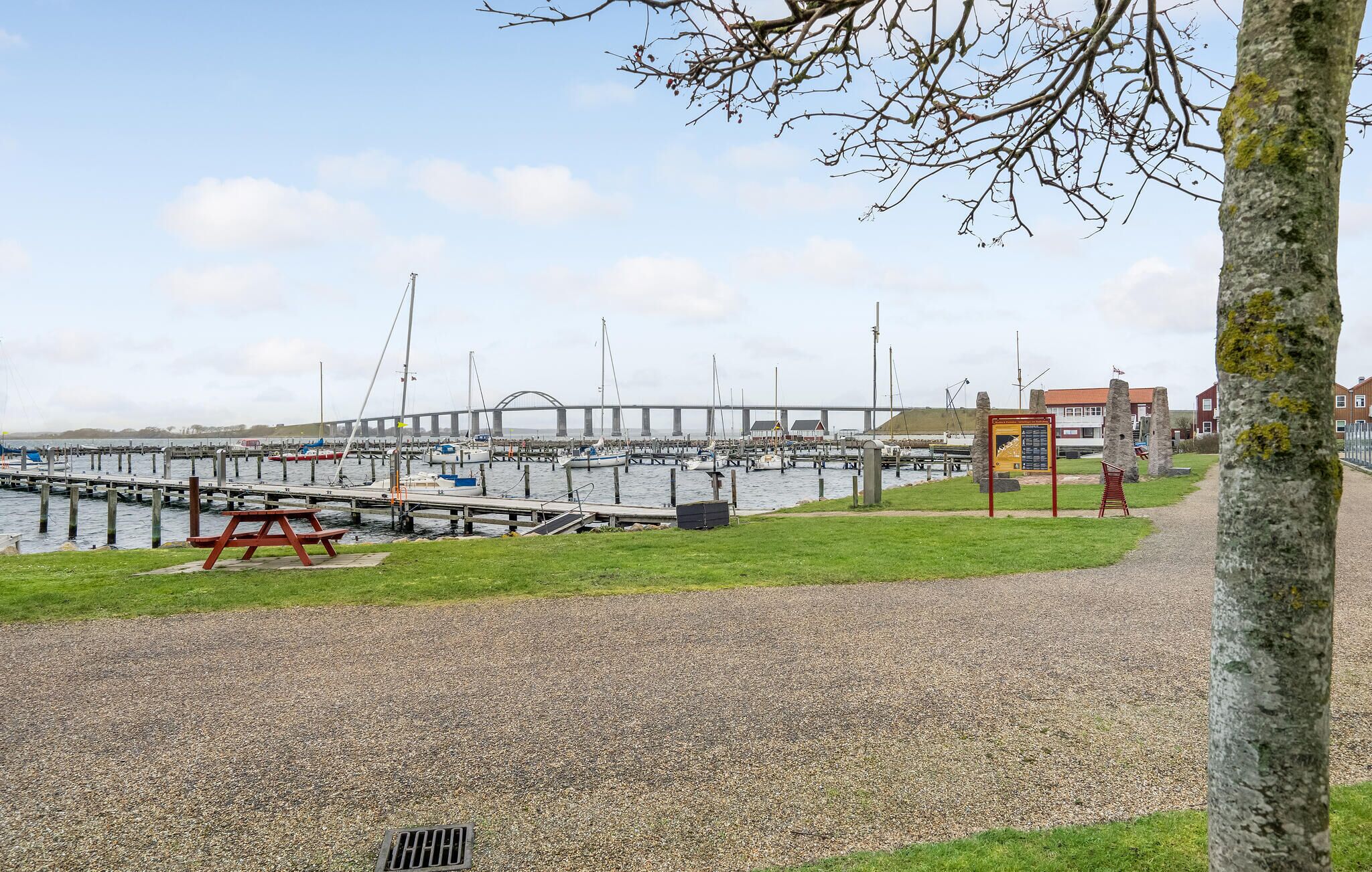 A marina with boats docked, a pedestrian path, and a bridge in the background.