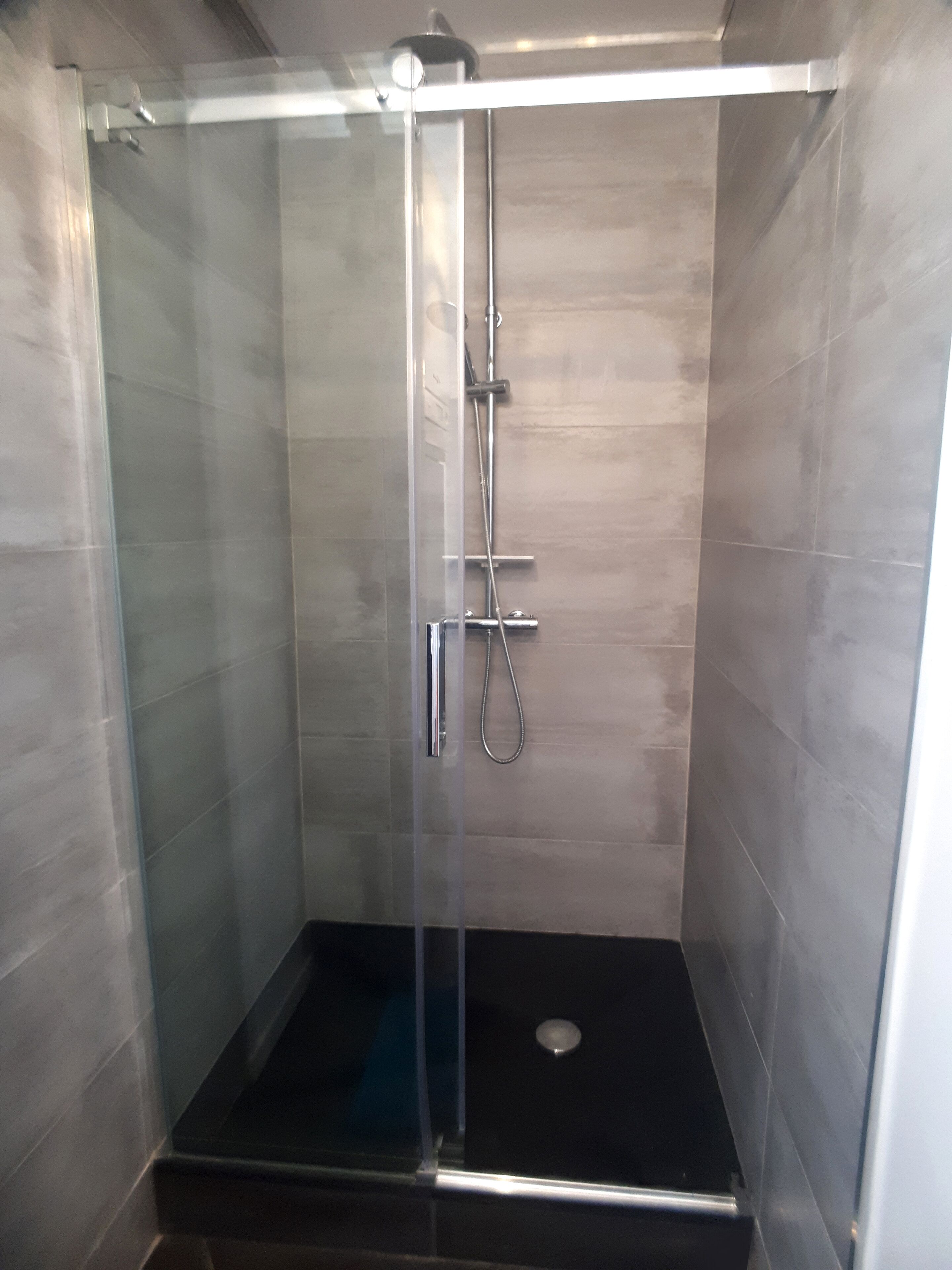Cabina de ducha con paredes de cristal, cabezal de ducha de mano y grifo empotrado.