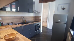 A modern kitchen with dark cabinets, a wooden countertop, a built-in oven, and a stainless steel refrigerator. - Ligny garden (ST OMER)