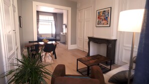 A living room with a sofa, a coffee table, a dining table with chairs, a fireplace, and a large plant. - Ligny garden (ST OMER)