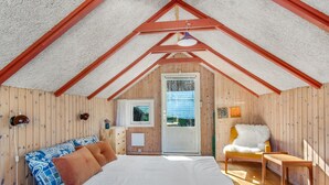A cozy attic bedroom with a wooden sloped ceiling, a bed with patterned pillows, a small table, and a chair. - 2 bedroom awesome home in Sejerø (Sejerø)