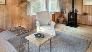 A cozy living room with a wooden interior, a comfortable armchair, a small table with a decorative bowl, and a fireplace. - 2 bedroom awesome home in Sejerø (Sejerø)
