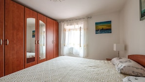 Una camera da letto con una coperta a motivi, un armadio in legno con specchi, una finestra con tende leggere e un quadro appeso al muro.