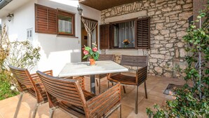 Un patio esterno con tavolo e sedie, pareti in pietra e una finestra con persiane.