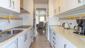 Una cucina piccola con mobili bianchi, un lavello in acciaio inox e una macchina da caffè Bosch.