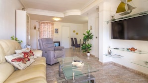 Un soggiorno con divano, poltrona, tavolino in vetro, televisore e oggetti decorativi.