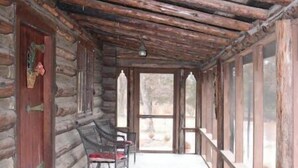 Una cabaña de troncos con porche, bancos de madera y chimenea de piedra.