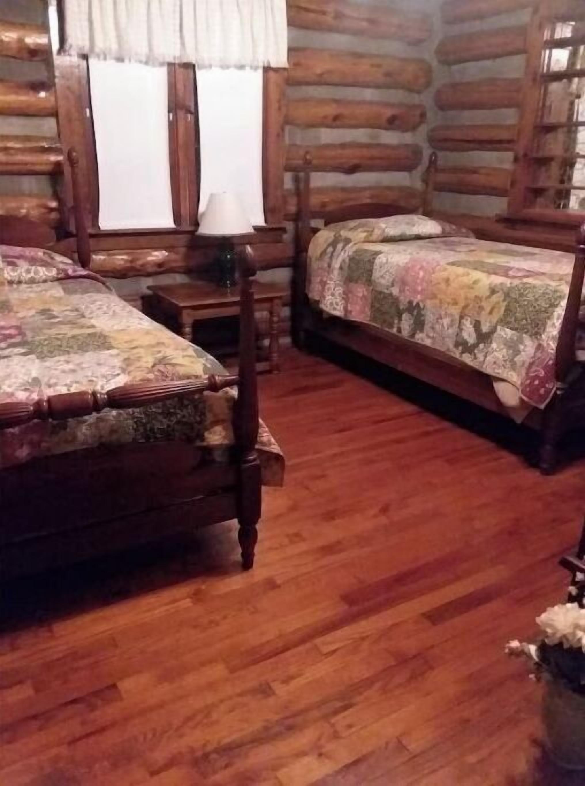 Habitació d'estil xalet de fusta amb dos llits de fusta, una taula de fusta i una finestra amb cortines.