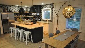 A modern kitchen with a central island, bar stools, a dining table, and a hanging light fixture. - Gorgeous Gem in Niagara’s Wine Country (Niagara Falls)
