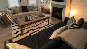 A living room with a sofa, coffee table, fireplace, and a TV mounted on the wall. - Gorgeous Gem in Niagara’s Wine Country (Niagara Falls)