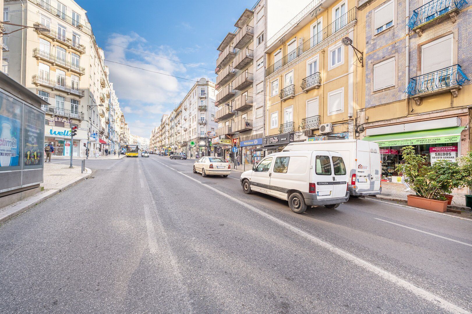 Une rue bordée d’immeubles, avec un autobus et des voitures.