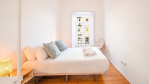 Quarto com cama, almofadas, uma cadeira e janela.