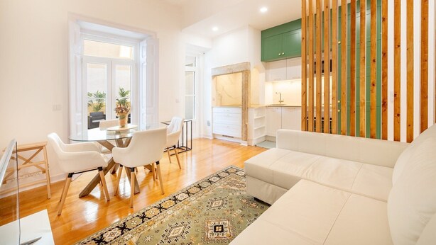 Uma sala de estar moderna com uma mesa de jantar de vidro, sofás brancos e um tapete estampado.