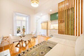 Uma sala de estar moderna com uma mesa de jantar de vidro, sofás brancos e um tapete estampado.