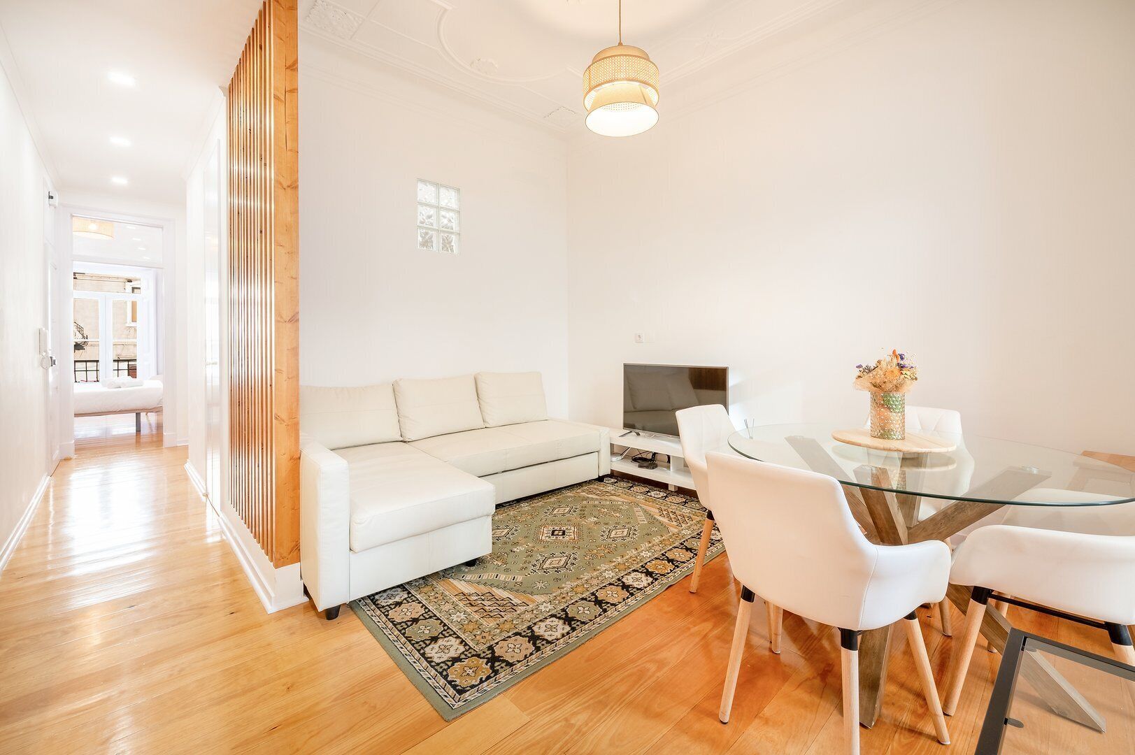 A modern living room with a white sofa, a glass dining table, and a TV.