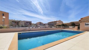 A swimming pool with a tiled deck, surrounded by buildings and a clear sky. - Amazing home in Agde with outdoor swimming pool (Agde)