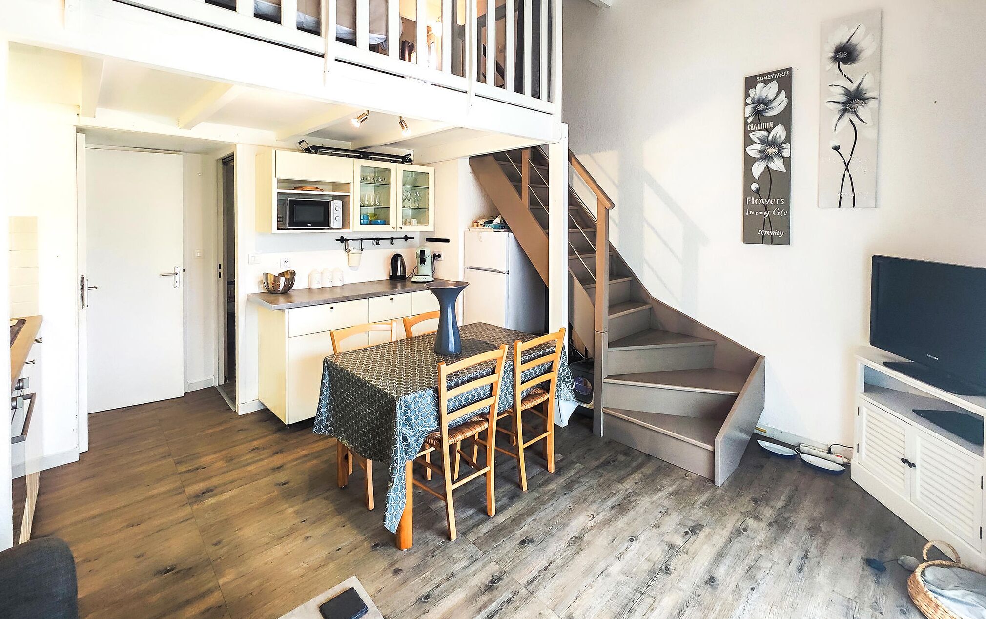 A compact living space with a kitchen, dining area, and a staircase leading to an upper level.