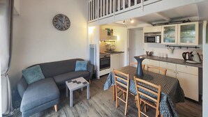 A compact living space with a sofa, a small table, a dining area with chairs, a kitchenette with a microwave, and a clock on the wall. - Amazing home in Agde with outdoor swimming pool (Agde)