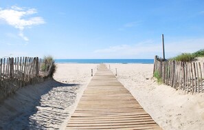 Ein hölzerner Steg führt zu einem Strand unter blauem Himmel.