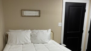 A neatly made bed with white bedding in a room with beige walls and a black door.