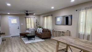 A spacious living room with a wooden coffee table, a sofa, a chair, and a dining table.