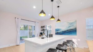 A modern kitchen with a central island, bar stools, pendant lighting, and a large window with a view. - Walk 2 Beach | Game Room | Firepit |Heat/Salt Pool (St. Augustine)