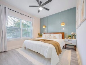 A bedroom with a bed, bedside tables, a ceiling fan, and a window with curtains. - Walk 2 Beach | Game Room | Firepit |Heat/Salt Pool (St. Augustine)