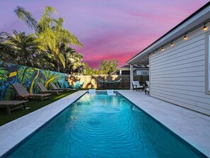 A rectangular swimming pool with a wooden deck on one side and a mural on the other. - Walk 2 Beach | Game Room | Firepit |Heat/Salt Pool (St. Augustine)