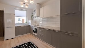 A modern kitchen with grey cabinets, white countertops, and a built-in oven. There is a stainless steel refrigerator on the left and a window above the sink. - Pet friendly home in Klodawa with sauna (Klodawa)