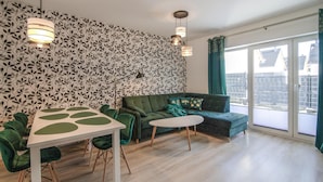 A modern living room with a patterned wallpaper, a green sofa, a white table with green accents, and a floor lamp. - Pet friendly home in Klodawa with sauna (Klodawa)