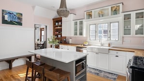 Una cocina moderna con armarios blancos, una isla central, sillas de madera y una araña.