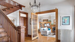 Una escalera de madera conduce a una sala de estar con un sofá blanco, un candelabro y un letrero que dice "HILL WORK METZ HOFFE".