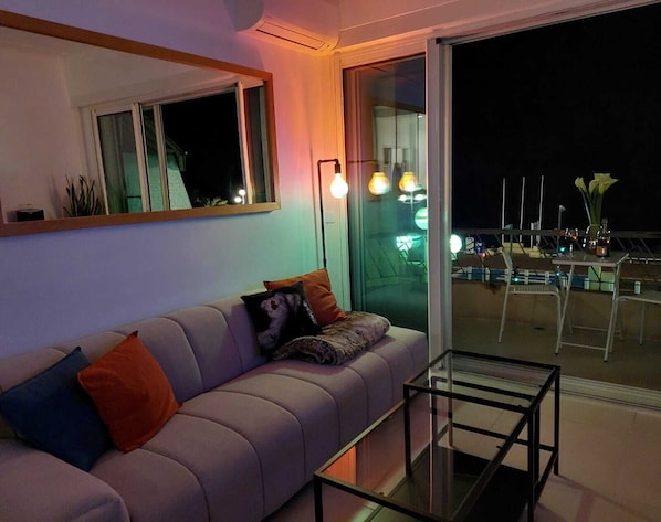 A modern living room with a sofa, a glass coffee table, and a large sliding glass door leading to an outdoor terrace.