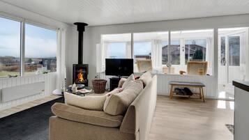 Relax in this spacious living room with a high ceiling, large windows, and a cozy wood-burning stove.