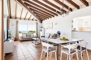 A spacious living area with a dining table, white chairs, a sofa, and a TV.