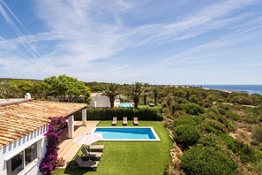 A pool with a view of the sea, a well-maintained lawn, and a building with a tiled roof.